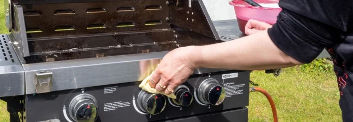 Person reinigt Gasgrill mit Tuch.